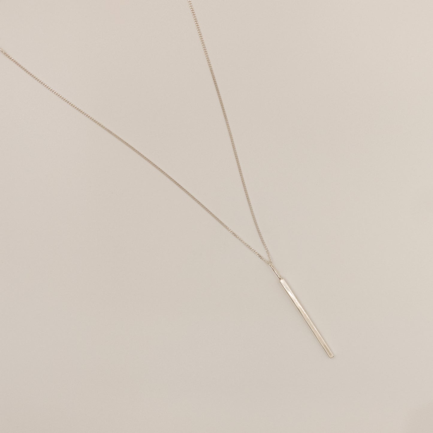 Top view of the Alignment silver bar pendant on a curb chain, pictured on a light plain background.