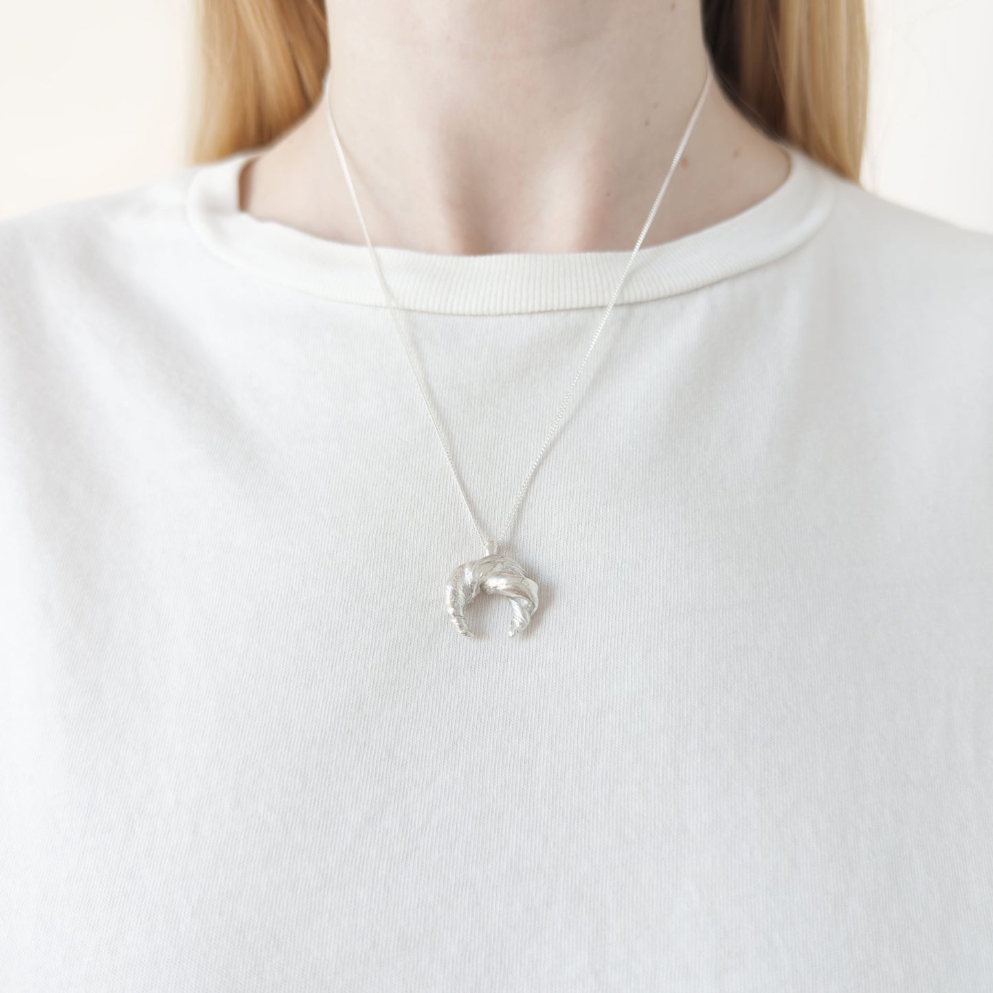Close up of the Arc silver necklace, featuring a textured pendant. Shown on a person wearing a white top.