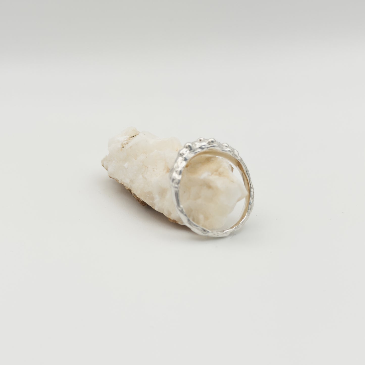 Side view of the Atoll textured silver ring, pictured on a light plain background next to a piece of beige rock.