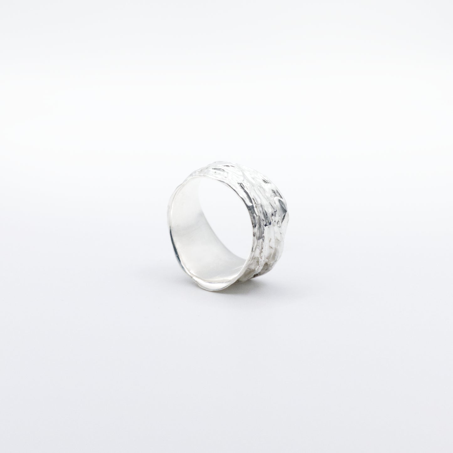Angled side view of the Canyon silver ring, pictured on a light plain background.