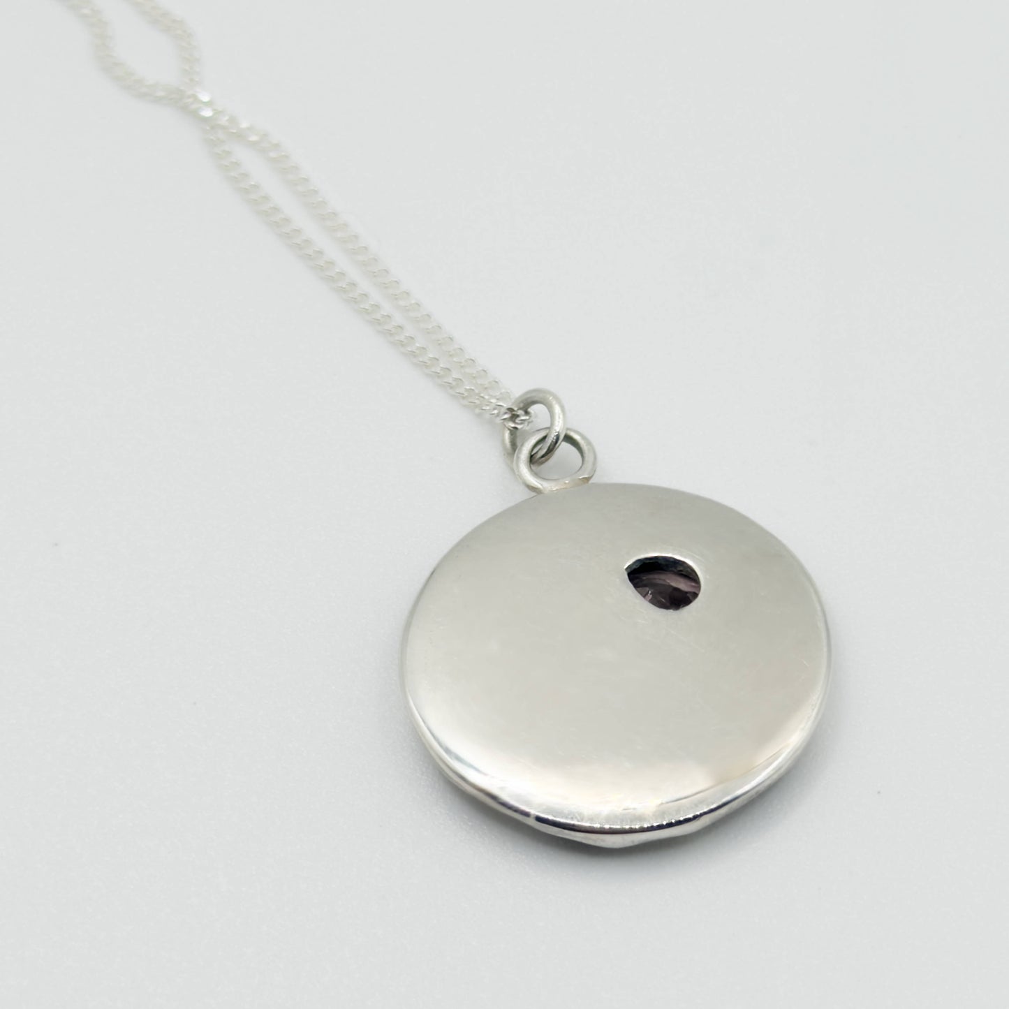 Angled back view of the Devotion silver necklace, featuring a round pendant. Pictured on a light plain background.