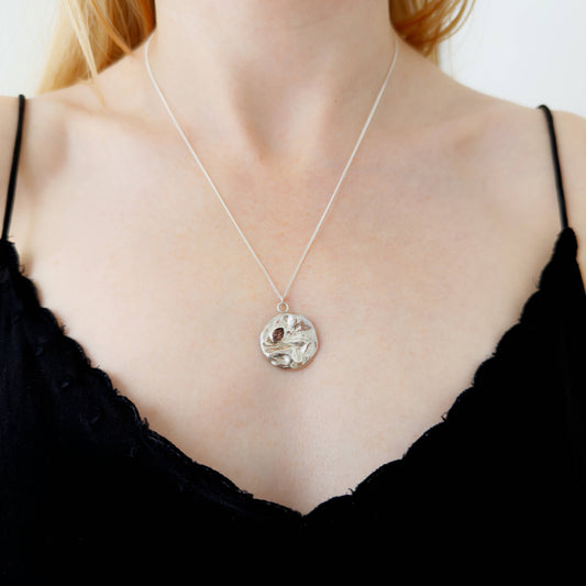 Close up of the Devotion silver necklace, featuring a round pendant. Shown on a person wearing a black top.