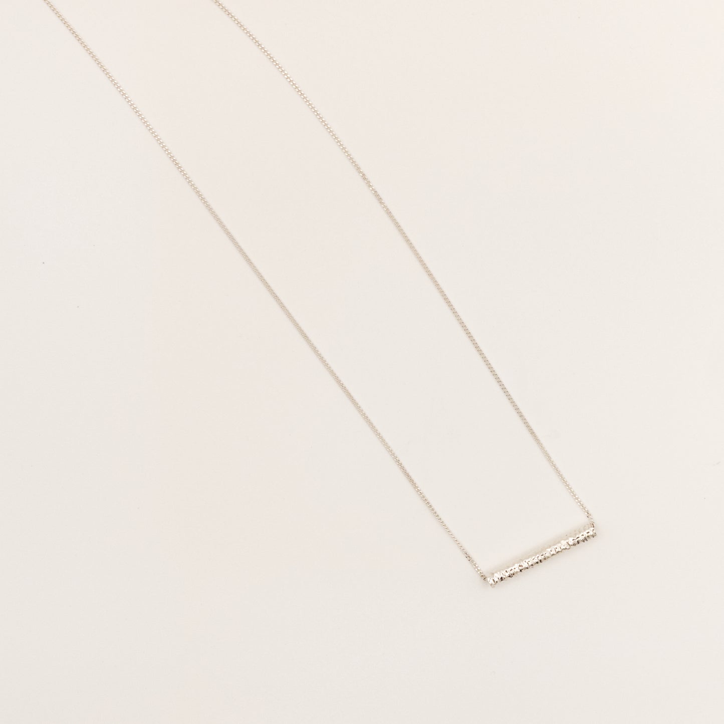 Top view of the Echo textured silver pendant on a curb chain, pictured on a light plain background.