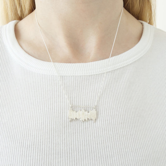 Close up of the Guidance silver necklace, featuring a textured pendant. Shown on a person wearing a white top.