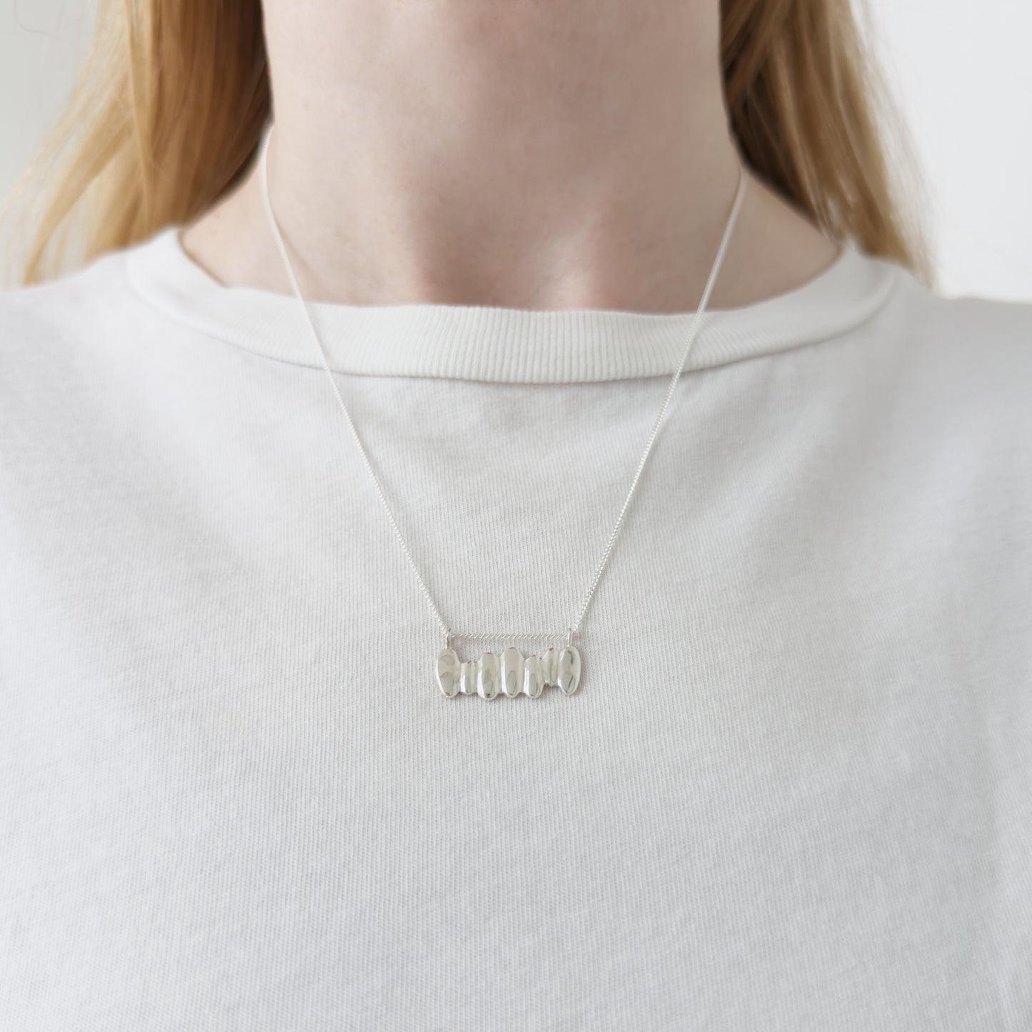 Close up of the Meridian textured silver necklace, featuring a textured pendant. Shown on a person wearing a white top.