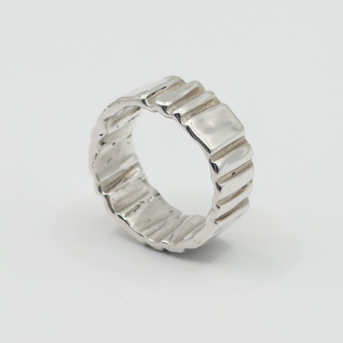 Angled side view of the Ripple silver ring, pictured on a light plain background.