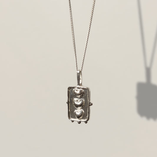 Angled front view of the Self-Compassion textured silver pendant on a curb chain, pictured on a light plain background.