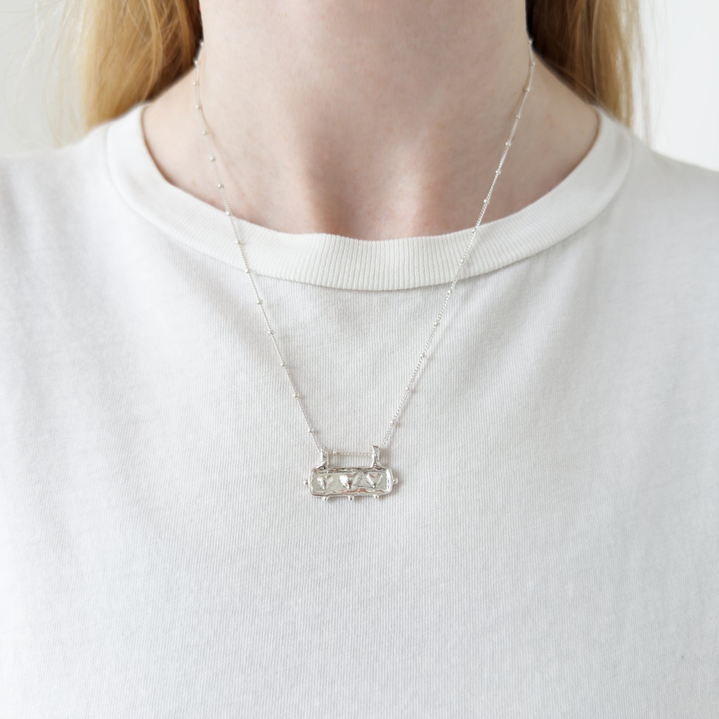 Self-Love textured silver pendant on a satellite chain. Pictured on a person wearing a white top.