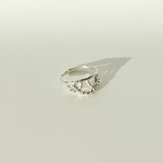 Angled front view of the Sequence textured silver ring, pictured on a light plain background.