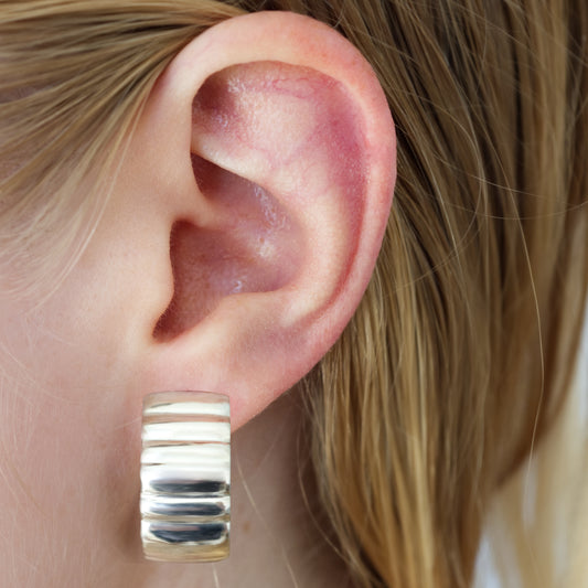 Close-up of an ear wearing the Wave Large silver hoop earring with blonde hair.
