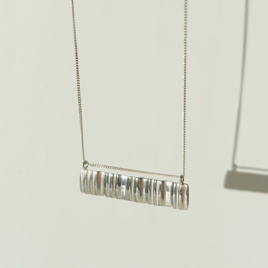 Angled front view of the Wave silver necklace with a textured rectangular pendant, pictured on a light plain background.