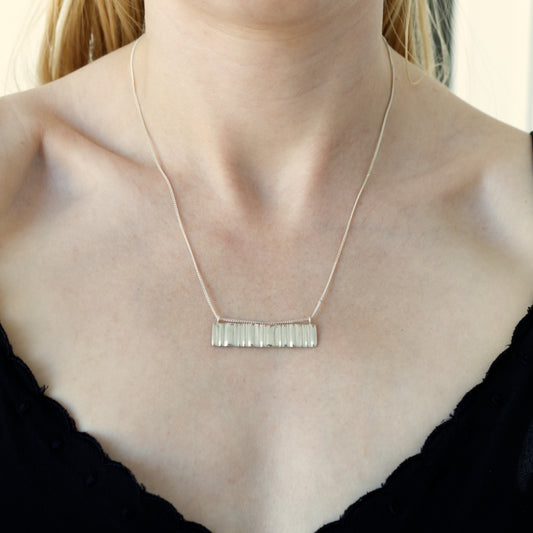 Close up of the Wave silver necklace, featuring a rectangular pendant. Shown on a person wearing a black top.
