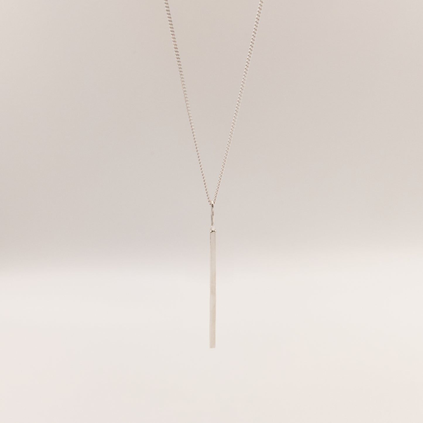 Front view of the Alignment silver bar pendant on a curb chain, pictured on a light plain background.