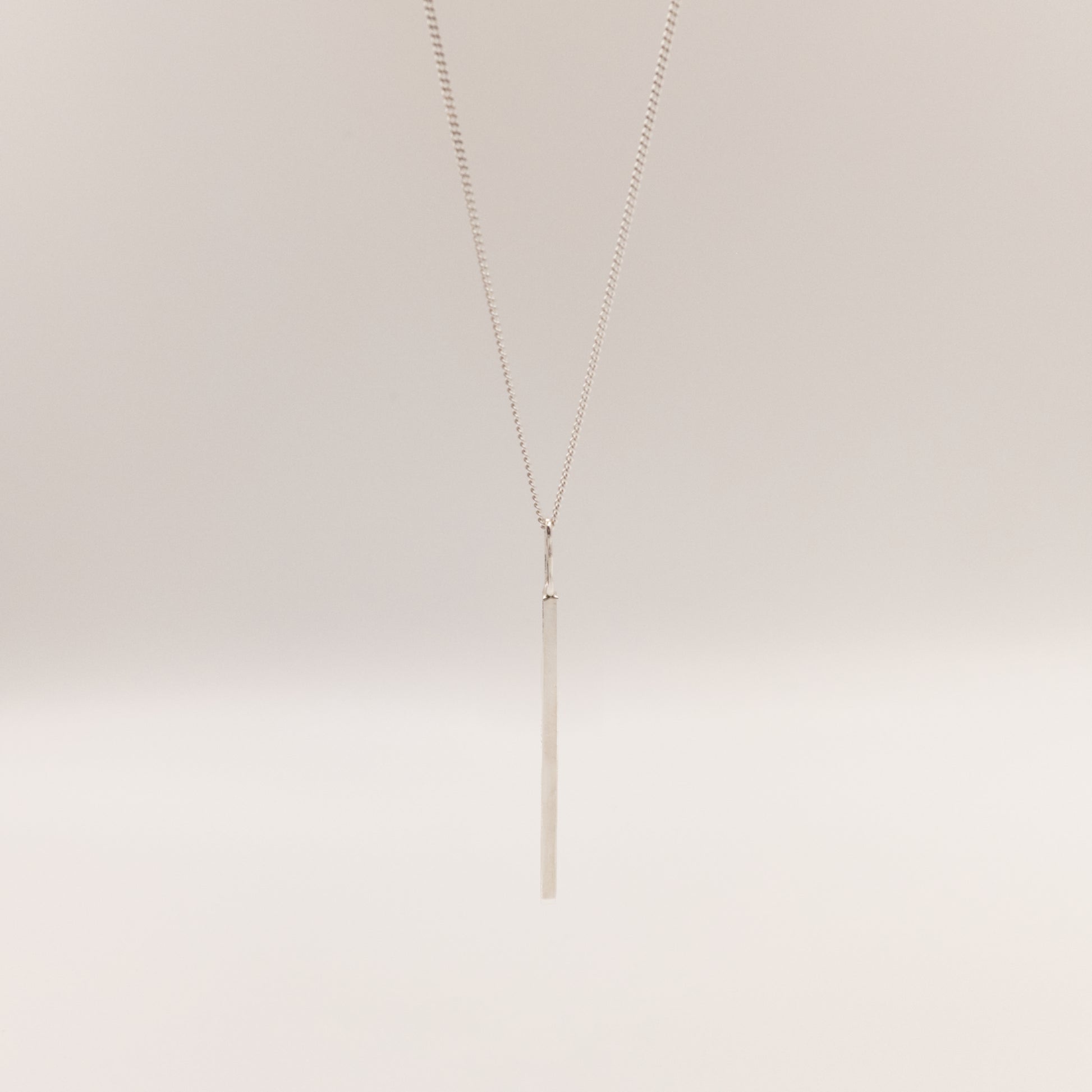 Front view of the Alignment silver bar pendant on a curb chain, pictured on a light plain background.