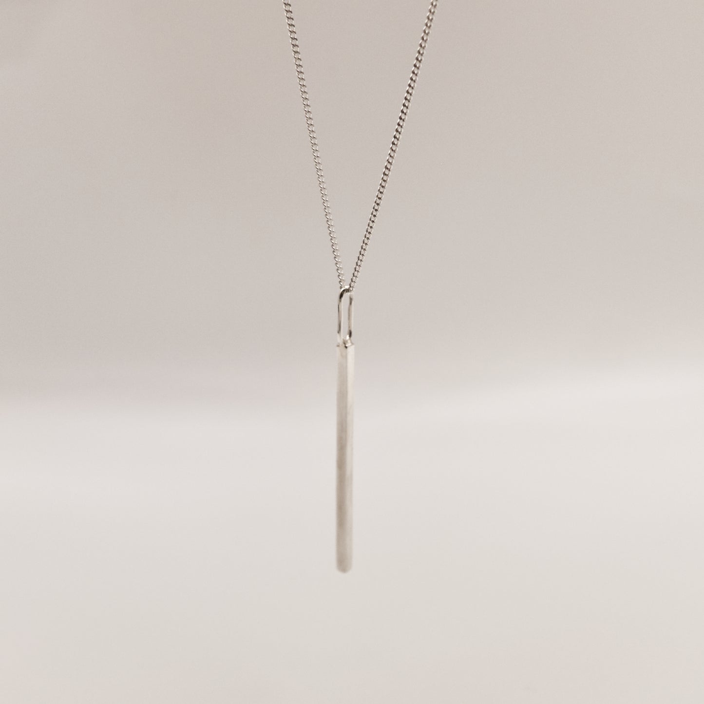 Angled front view of the Alignment silver bar pendant on a curb chain, pictured on a light plain background.
