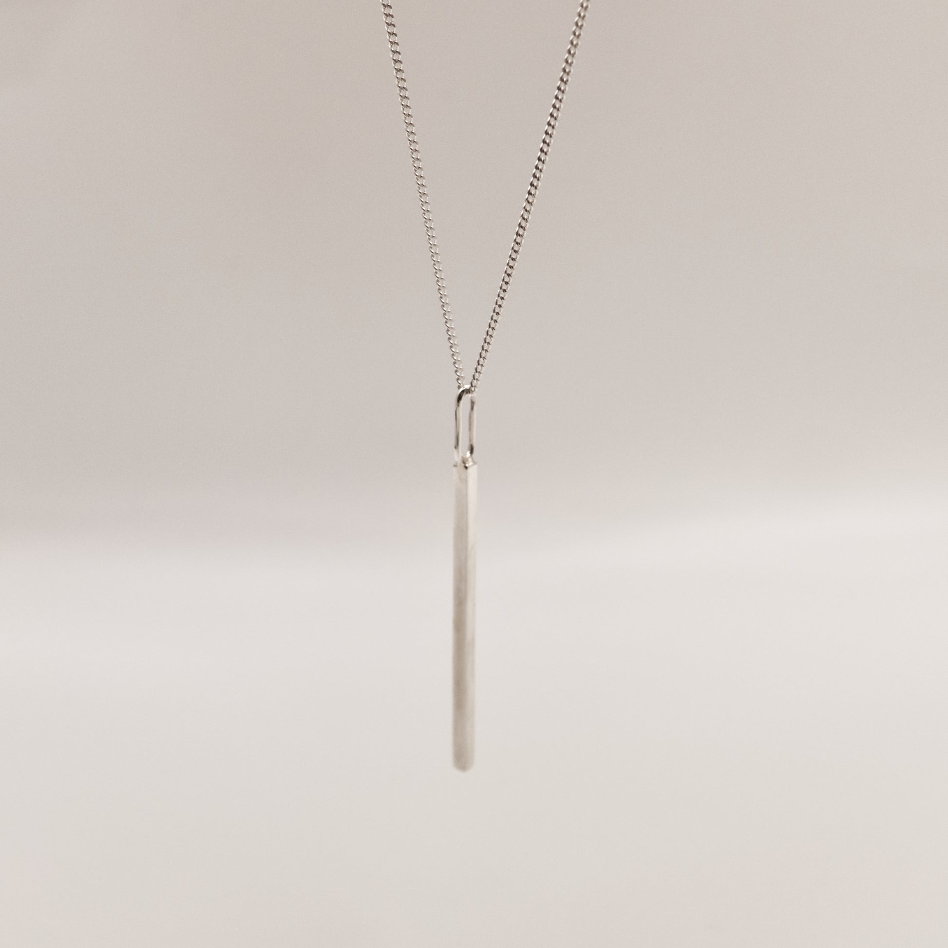 Angled front view of the Alignment silver bar pendant on a curb chain, pictured on a light plain background.