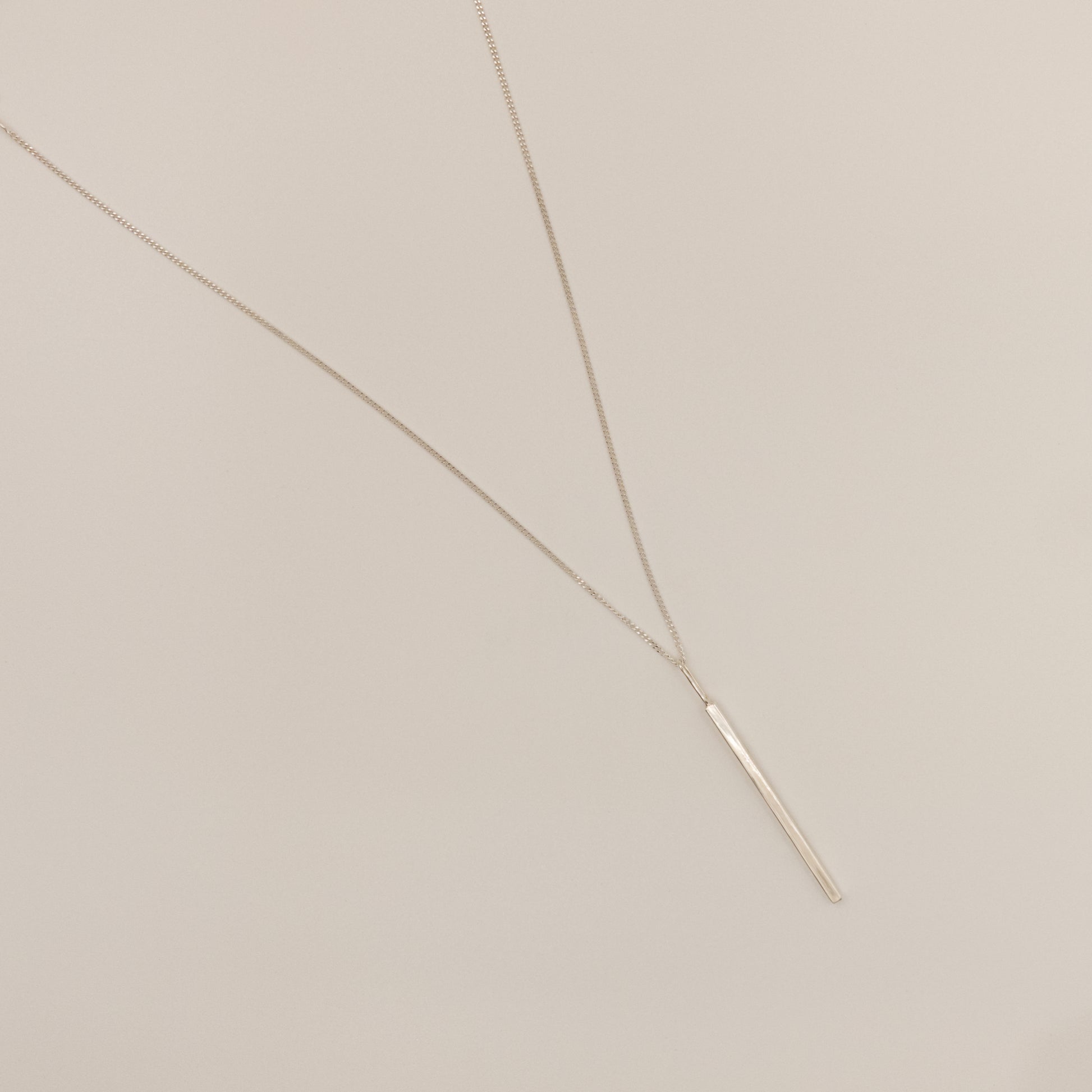 Top view of the Alignment silver bar pendant on a curb chain, pictured on a light plain background.