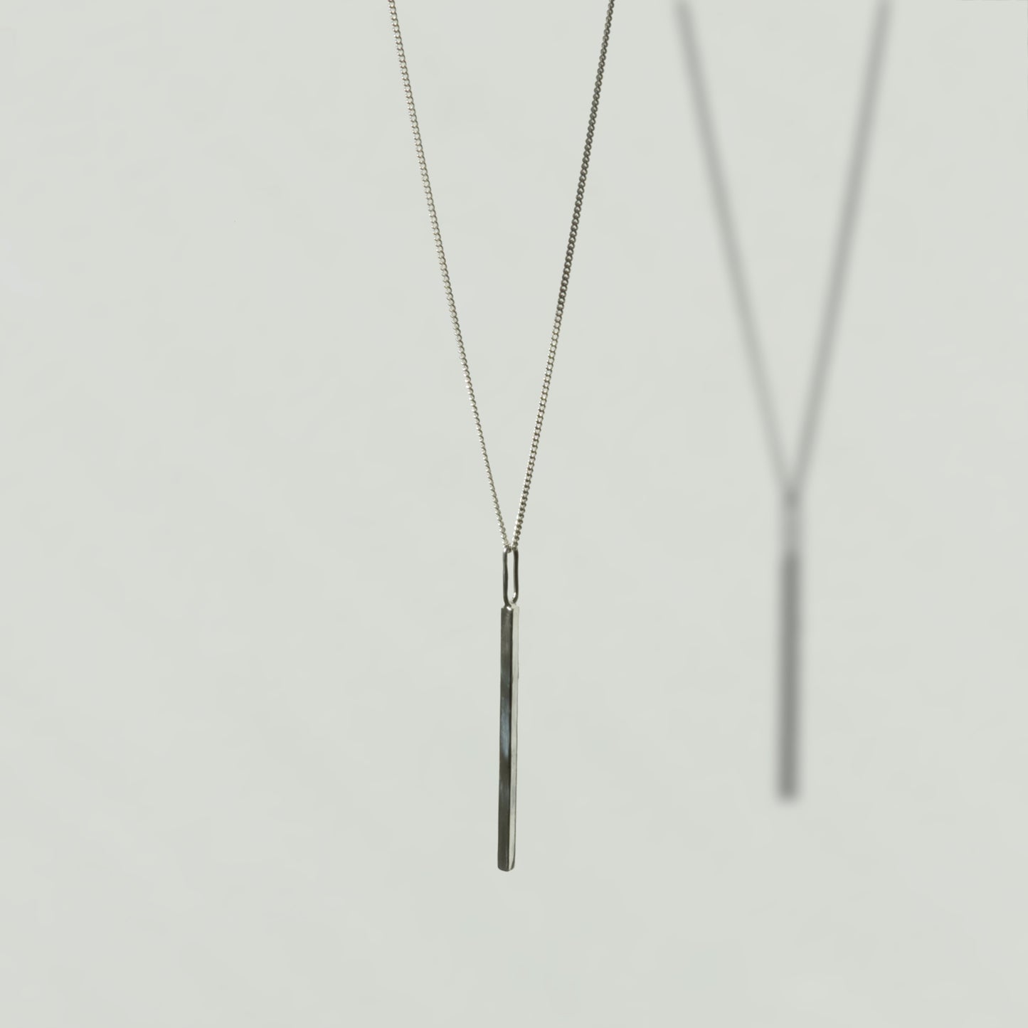 Angled front view of the Alignment silver bar pendant on a curb chain, pictured on a light plain background.