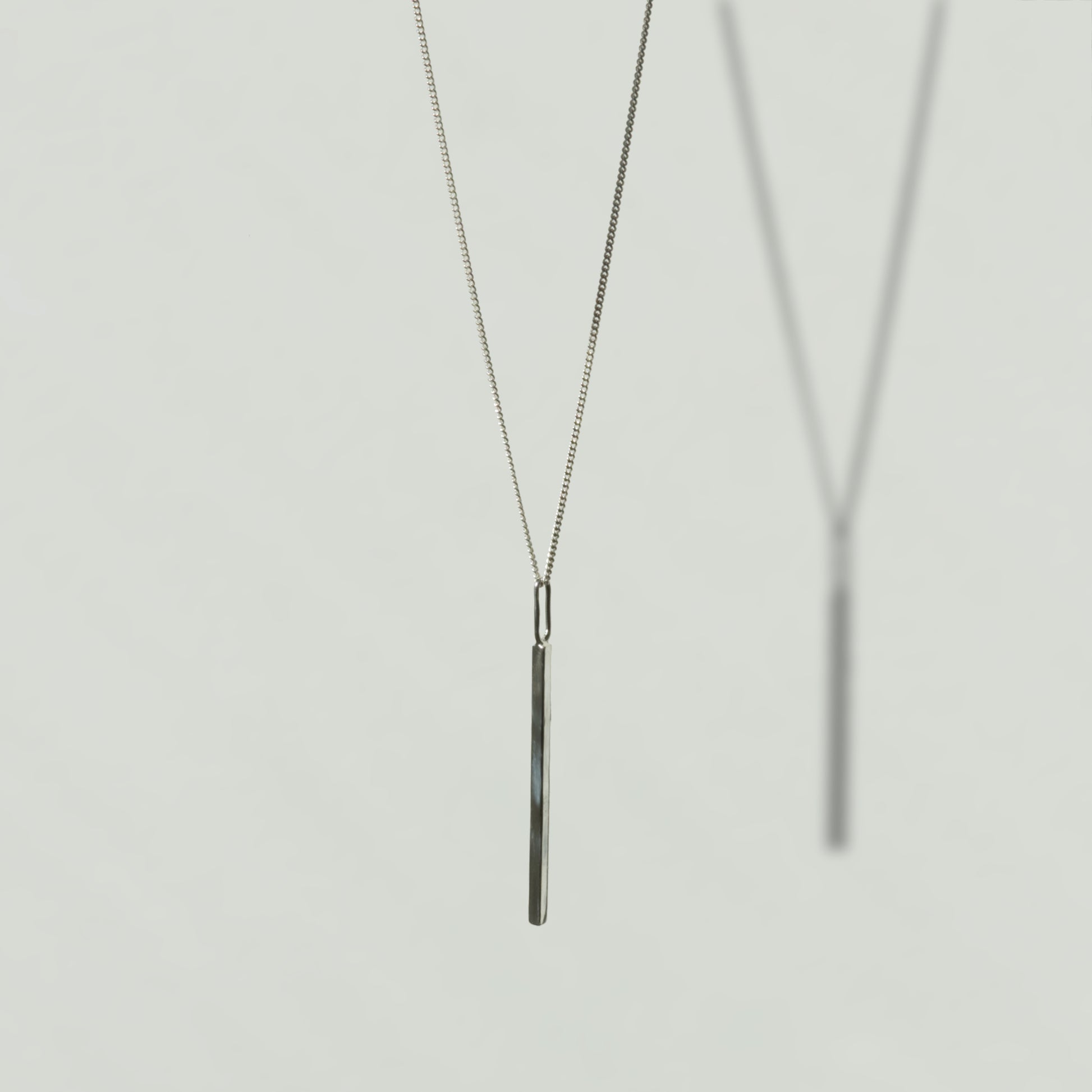 Angled front view of the Alignment silver bar pendant on a curb chain, pictured on a light plain background.