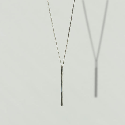 Angled front view of the Alignment silver bar pendant on a curb chain, pictured on a light plain background.