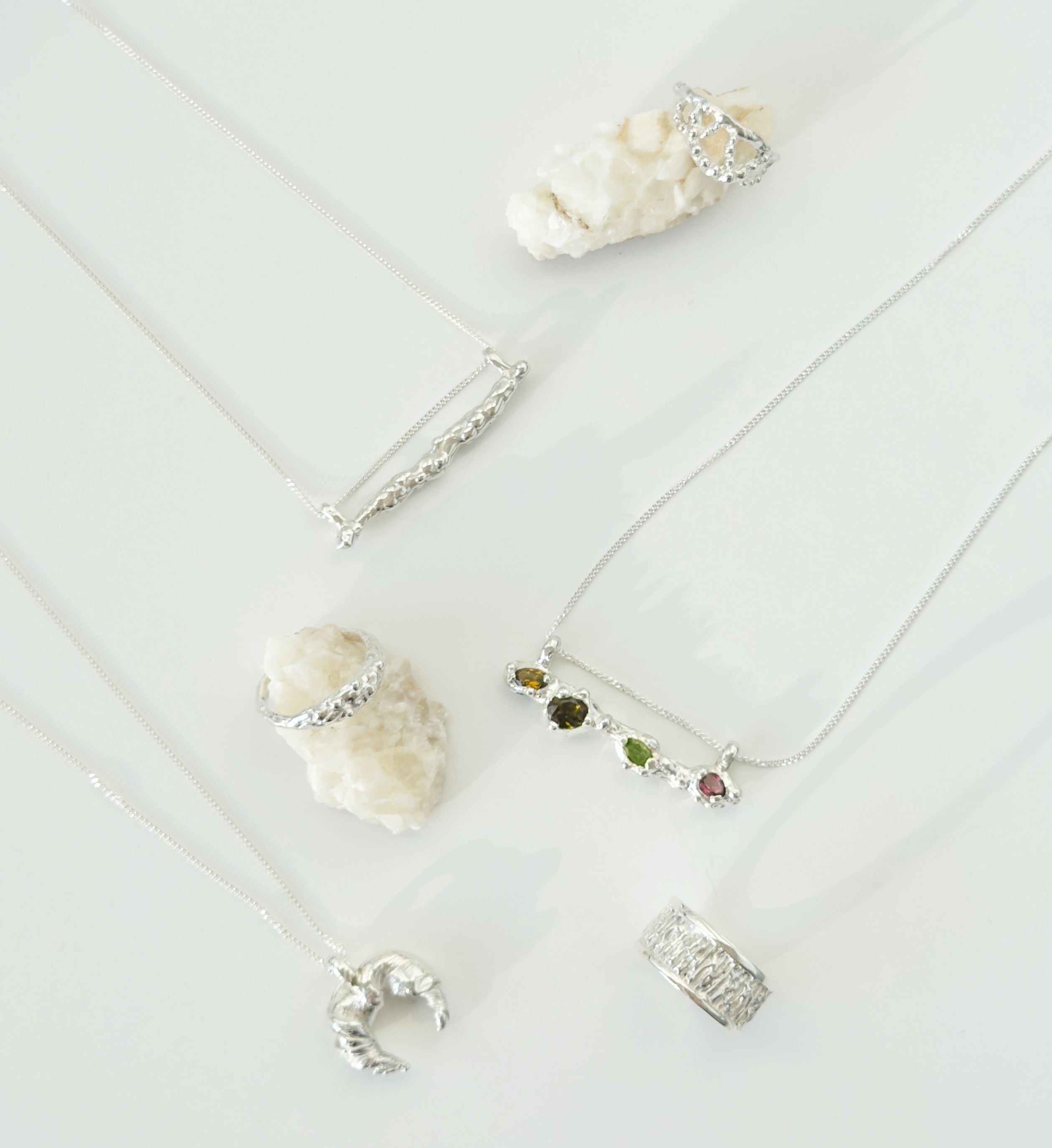 Collection of three silver necklaces with various pendants and three textured silver rings on a white surface.