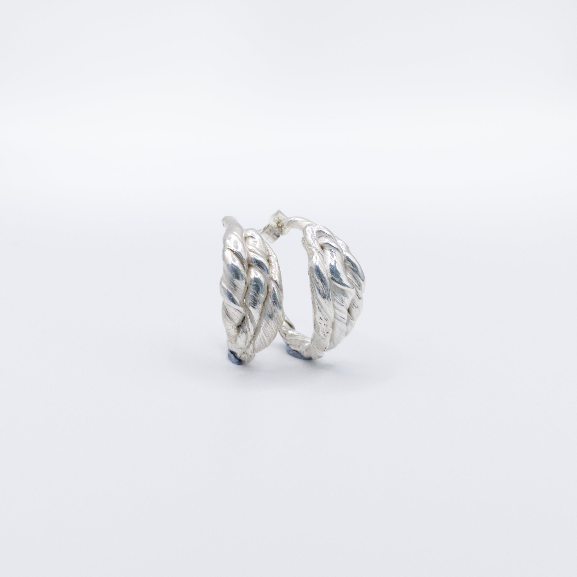 Angled front view of a pair of Anchor silver hoop earrings, pictured on a light plain background.