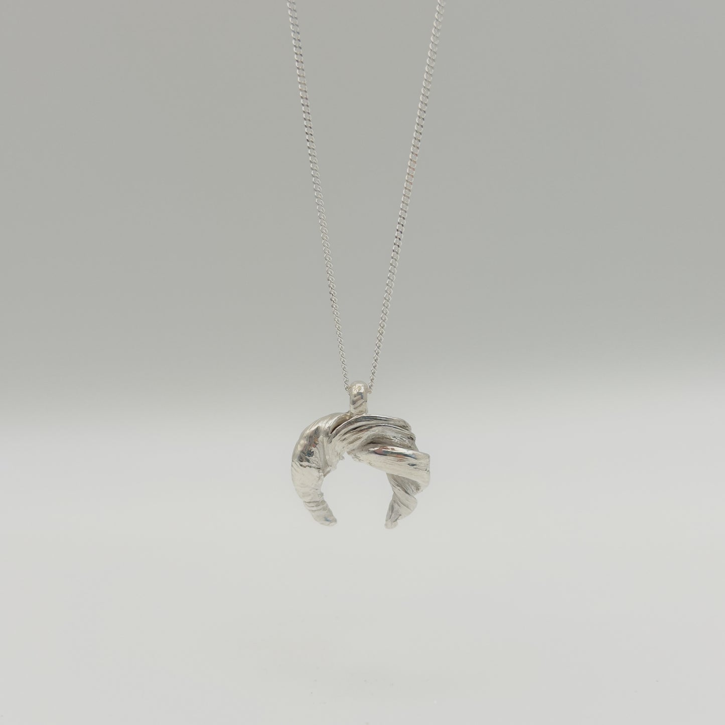 Front view of the Arc textured silver pendant on a chain, pictured on a light plain background.