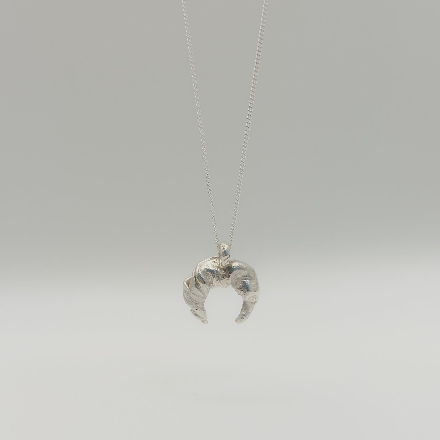 Back view of the Arc textured silver pendant on a chain, pictured on a light plain background.