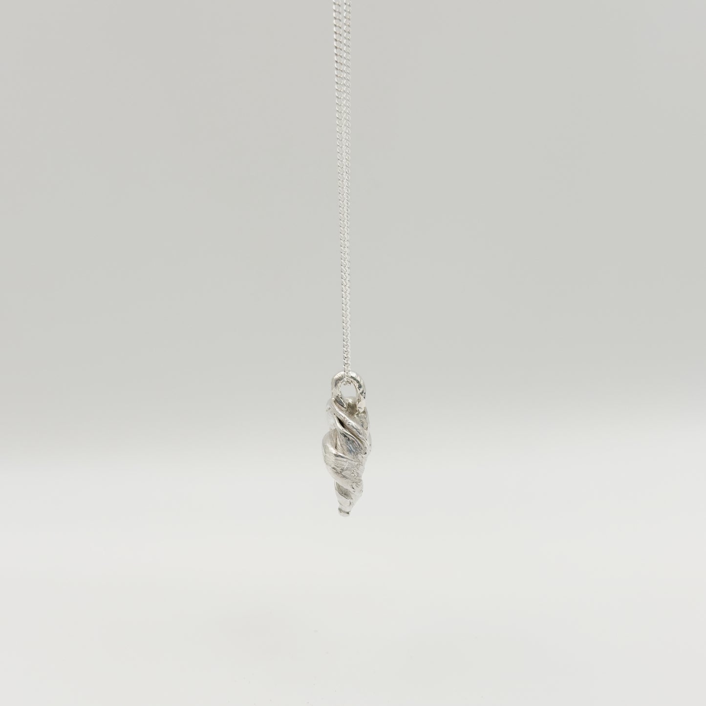 Side view of the Arc textured silver pendant on a chain, pictured on a light plain background.