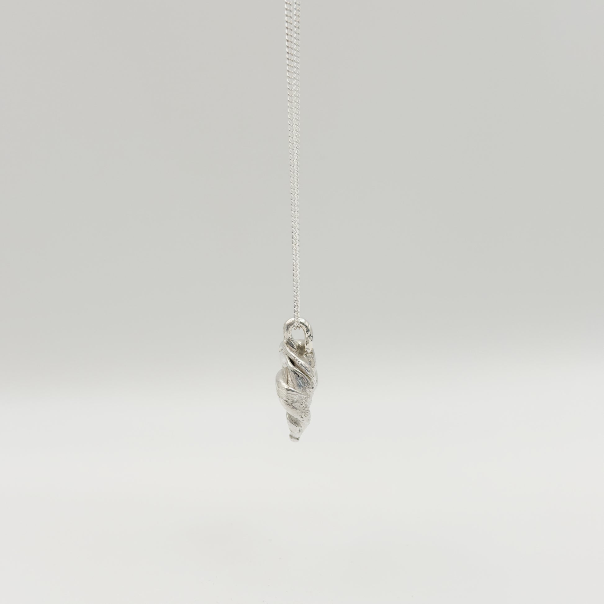 Side view of the Arc textured silver pendant on a chain, pictured on a light plain background.