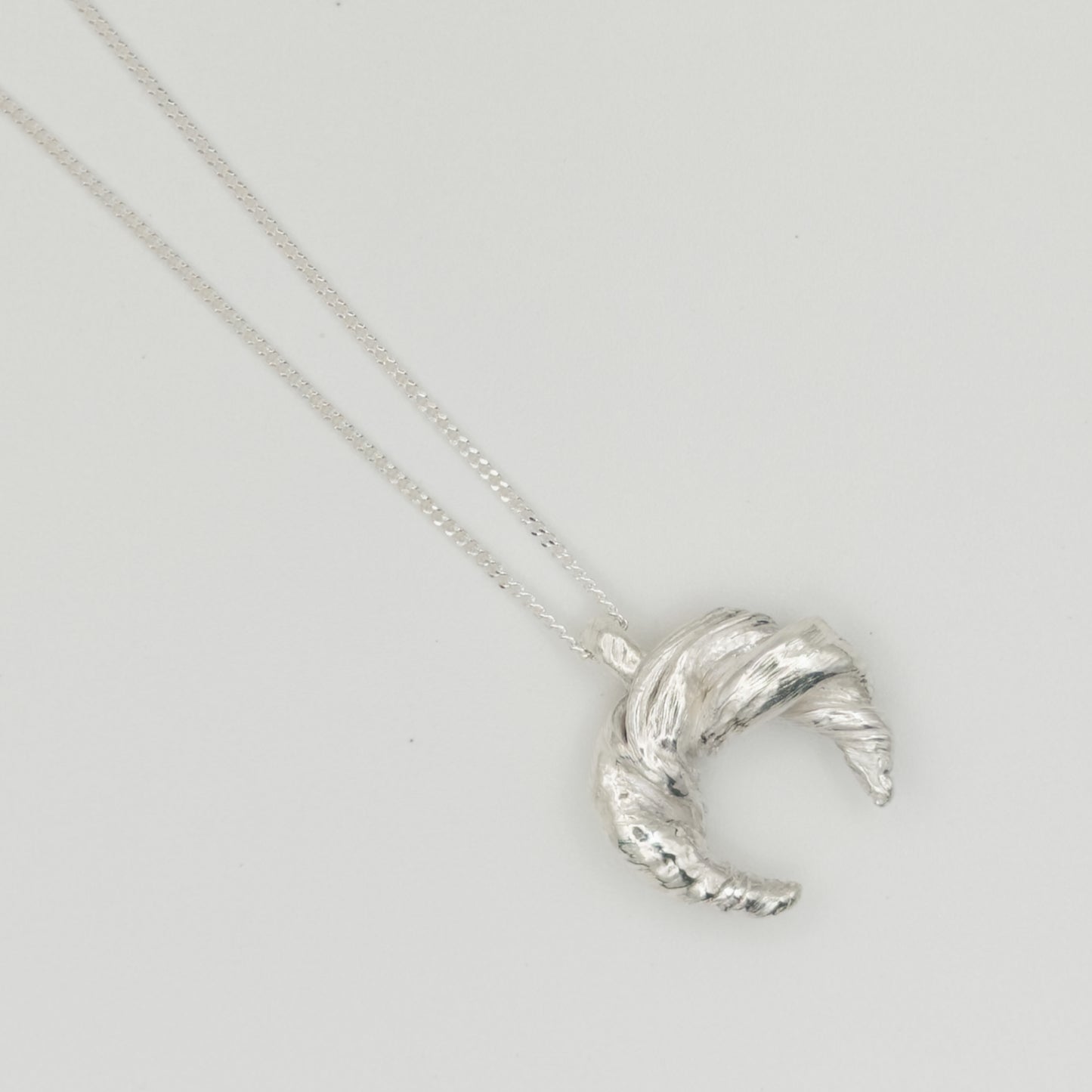 Enlarged top view of the Arc textured silver pendant on a chain, pictured on a light plain background.