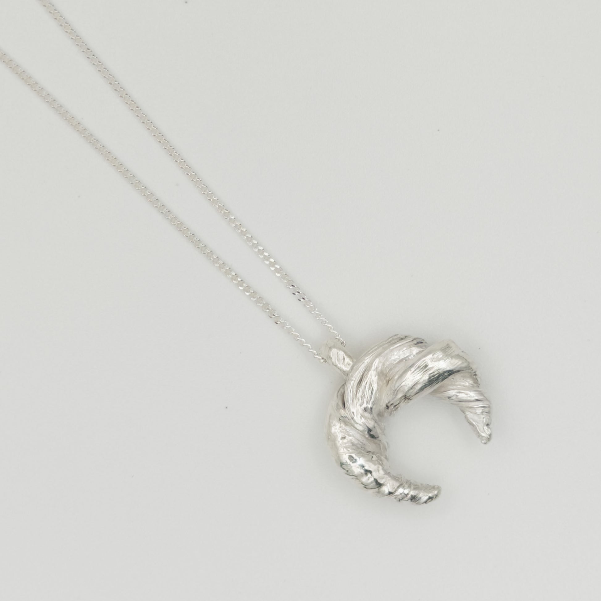 Enlarged top view of the Arc textured silver pendant on a chain, pictured on a light plain background.