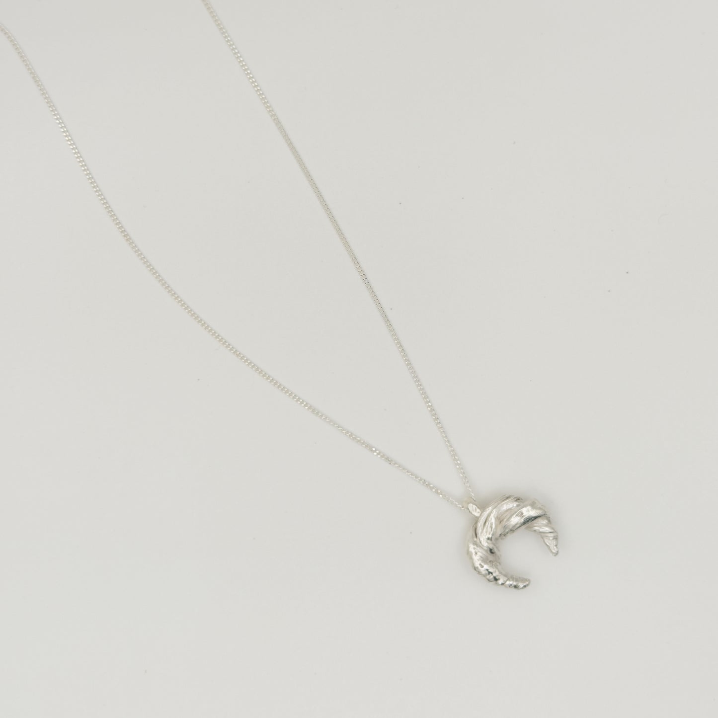 Top view of the Arc textured silver pendant on a chain, pictured on a light plain background.