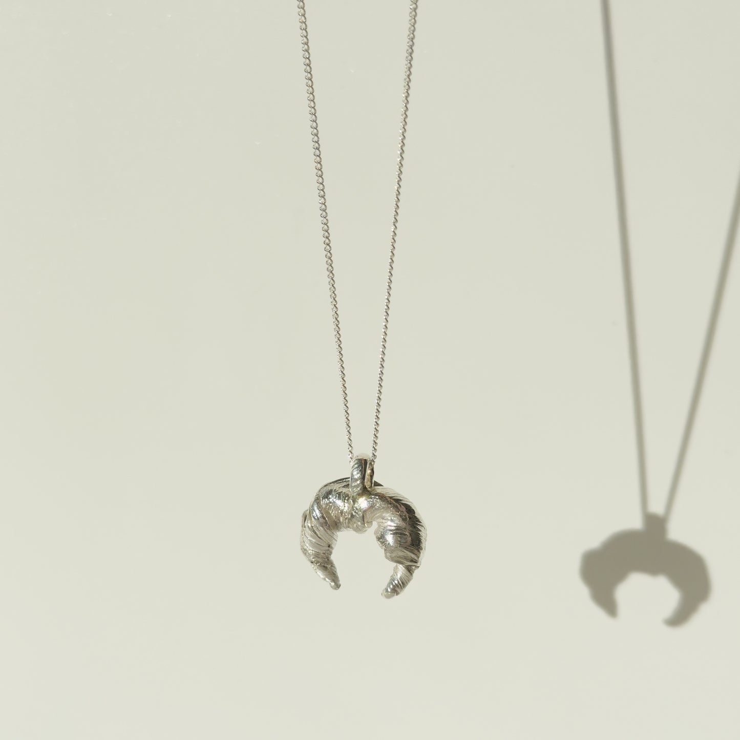 Angled front view of the Arc textured silver pendant on a chain, pictured on a light plain background.