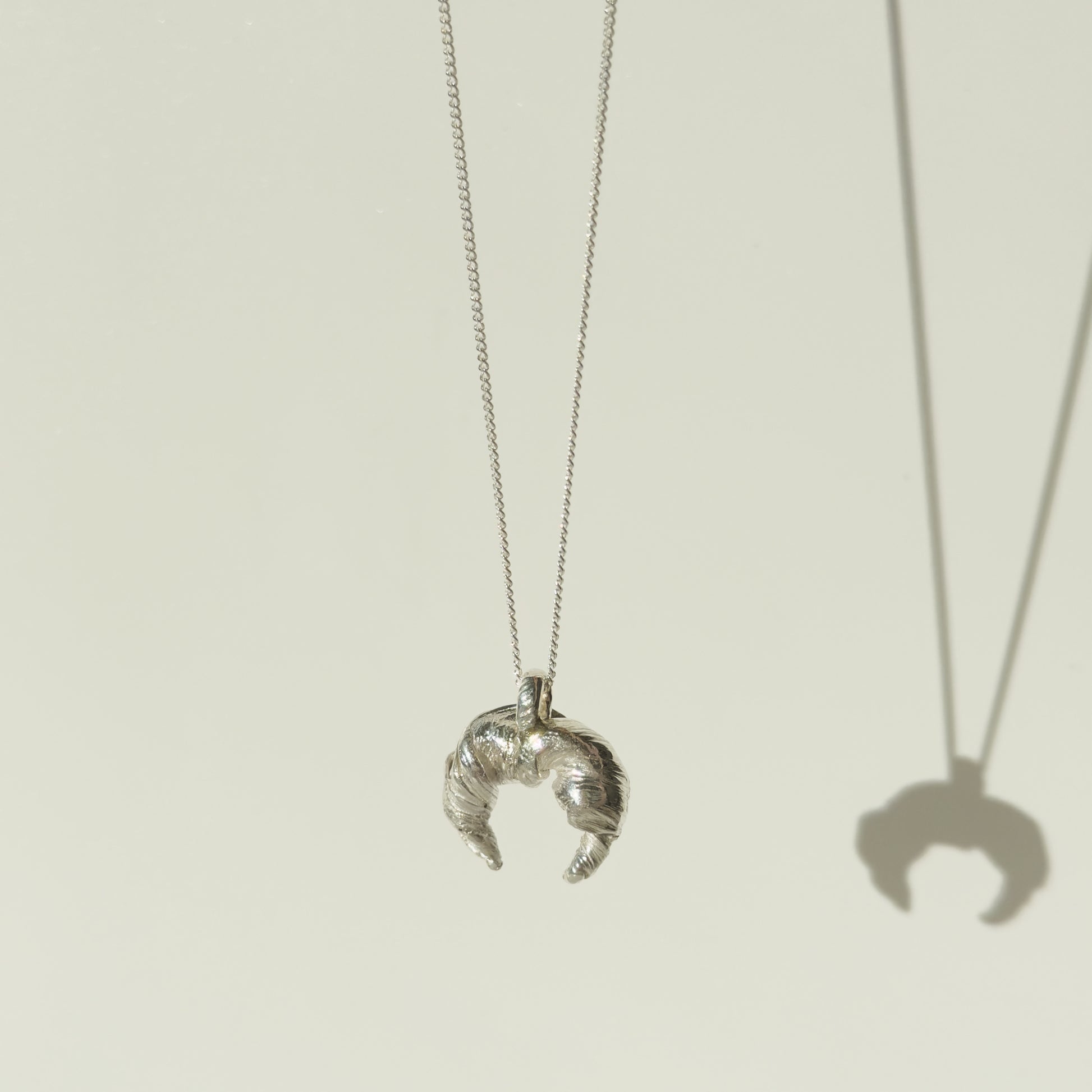 Angled front view of the Arc textured silver pendant on a chain, pictured on a light plain background.