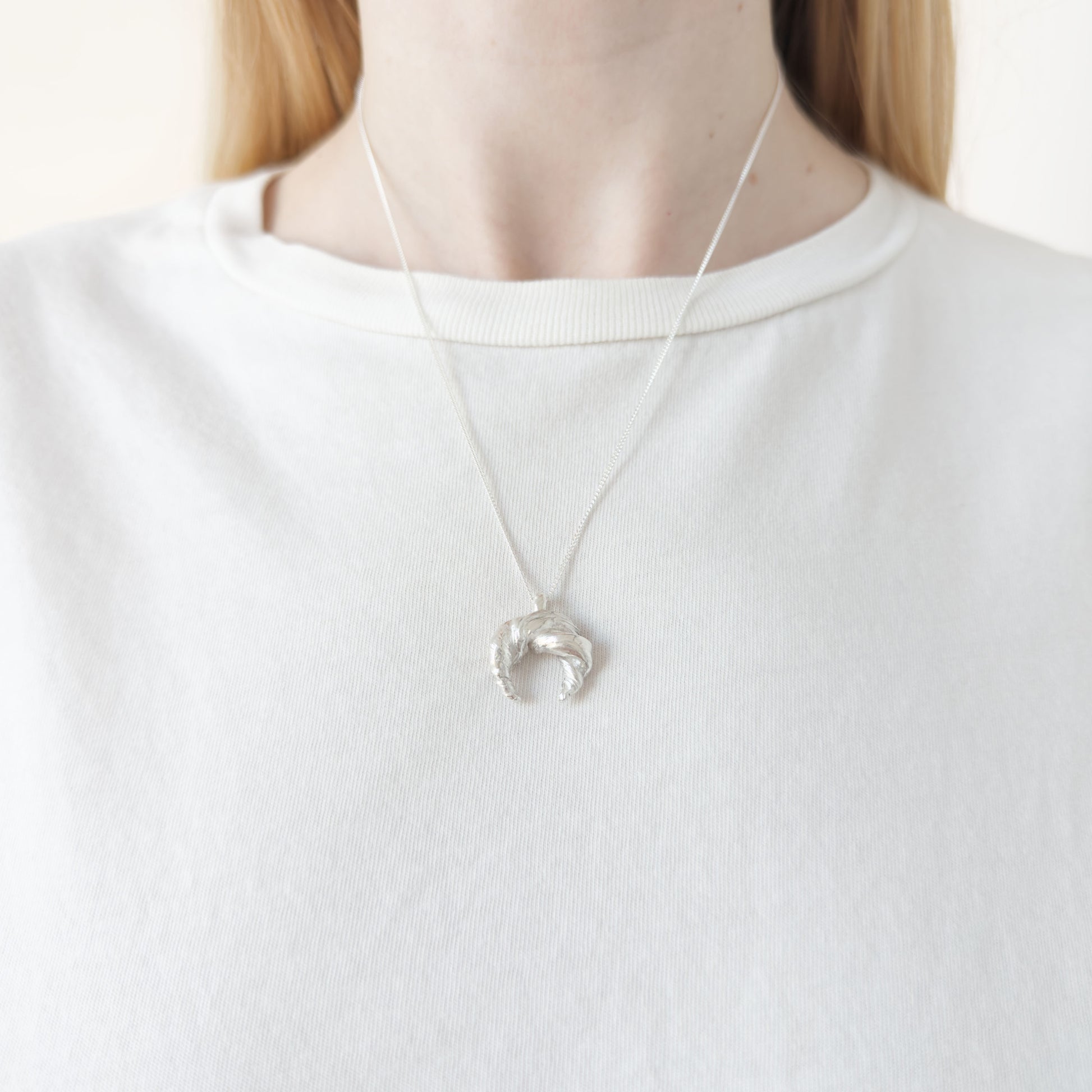 Close up of the Arc silver necklace, featuring a textured pendant. Shown on a person wearing a white top.