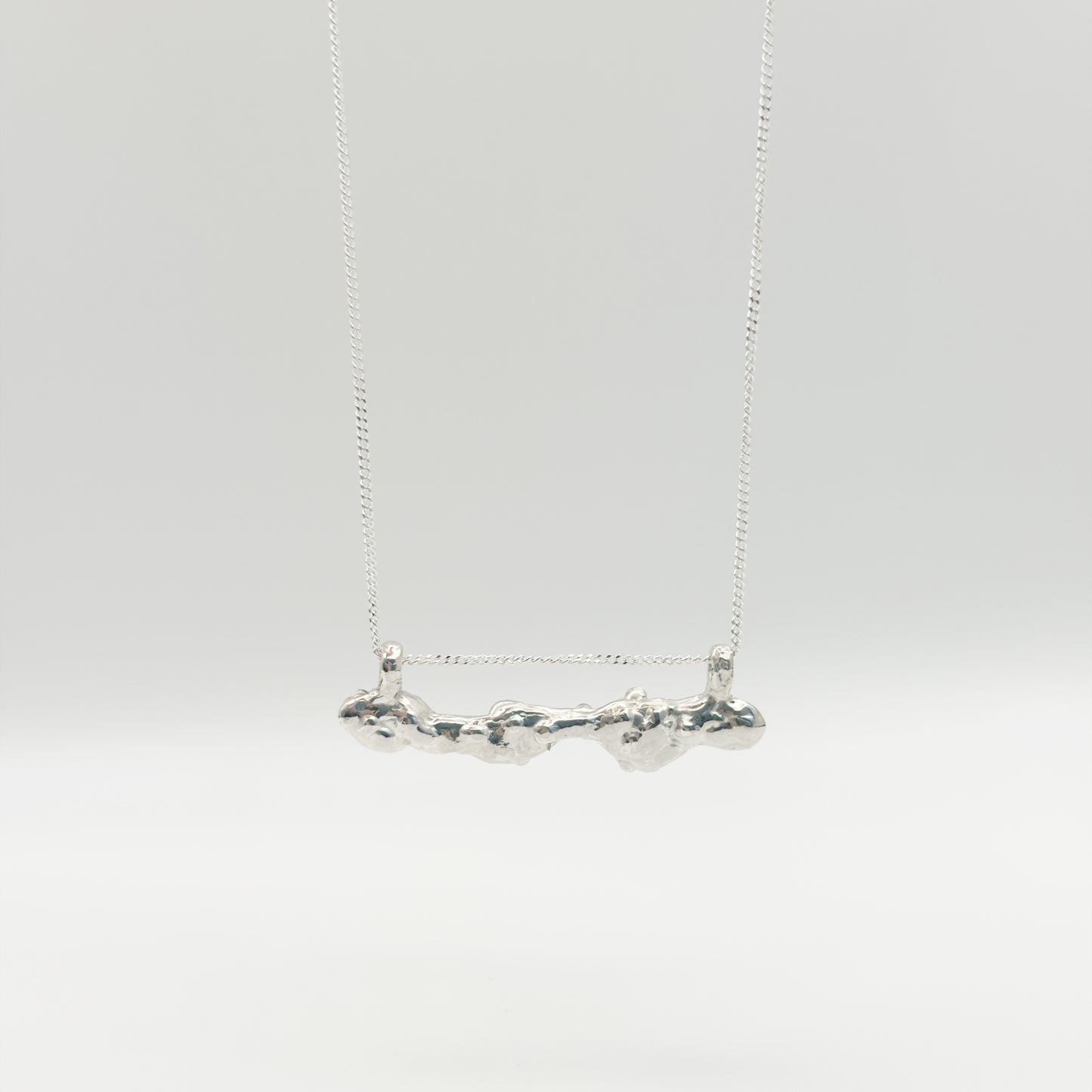 Back view of the Atoll Editions No1 silver necklace, featuring a textured bar pendant. Shown on a plain light background.
