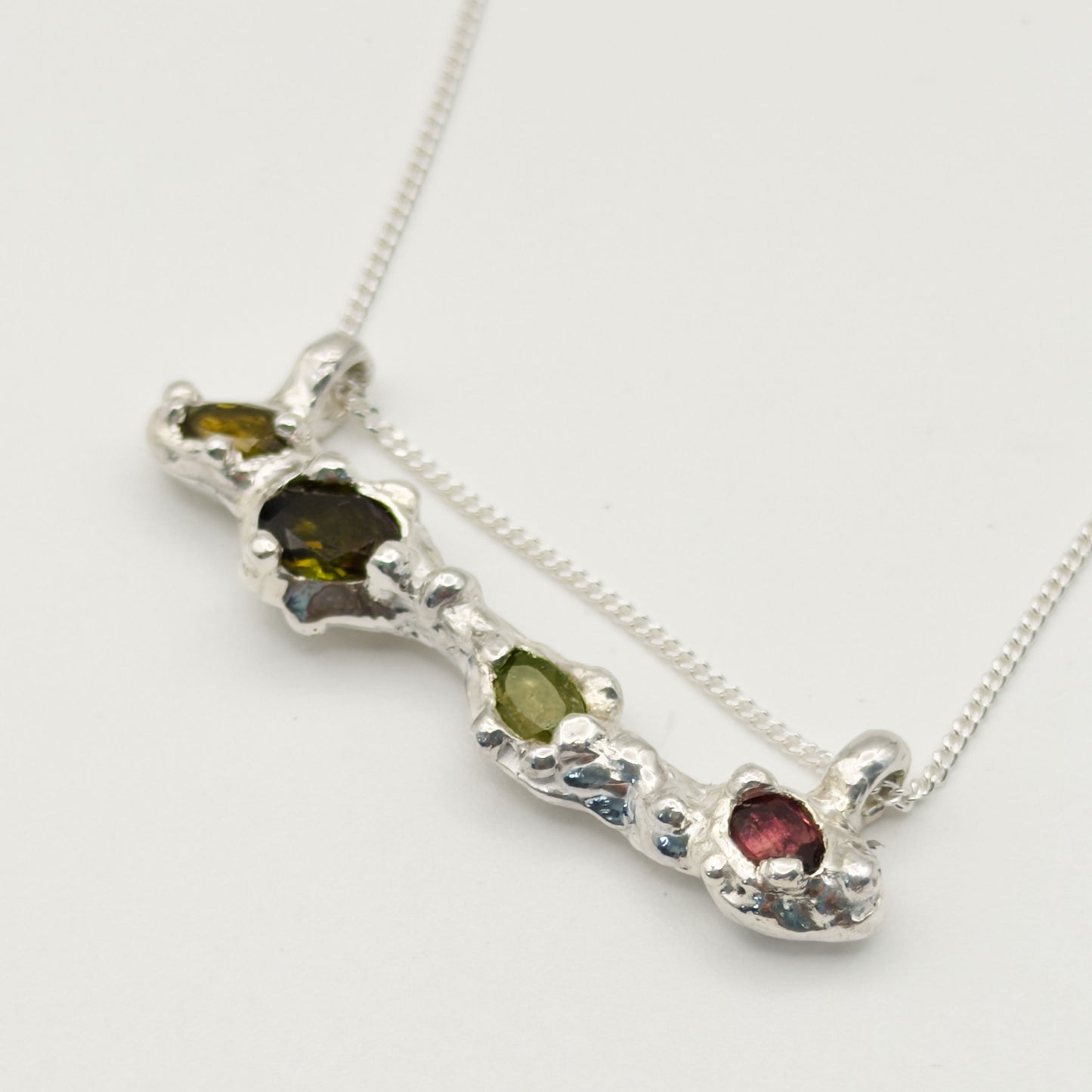 Close up of the Atoll Editions No1 silver necklace, featuring a textured bar pendant with multicolored tourmalines. Shown on a plain light background.