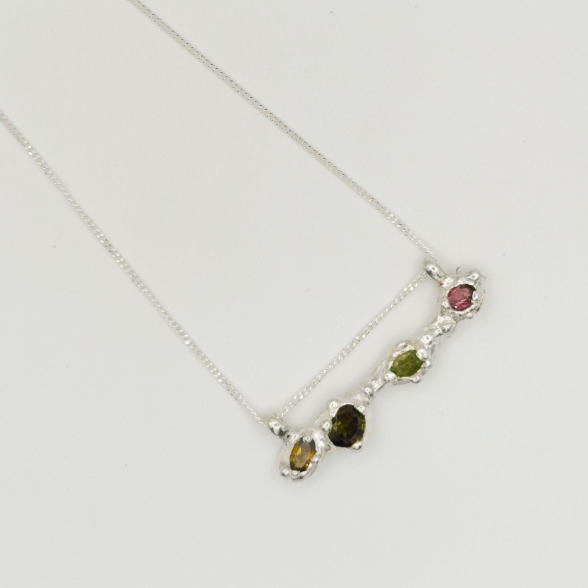 Top view of the Atoll Editions No1 silver necklace, featuring a textured bar pendant with multicolored tourmalines. Shown on a plain light background.