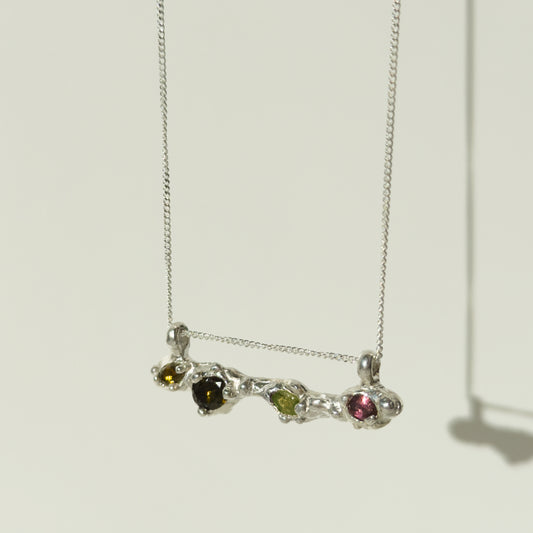 Angled front view of the Atoll Editions No1 silver necklace, featuring a textured bar pendant with multicolored tourmalines. Shown on a plain light background.
