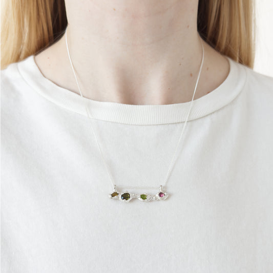 Close up of the Atoll Editions No1 silver necklace, featuring a textured bar pendant with multicolored tourmalines. Shown on a person wearing a white top.