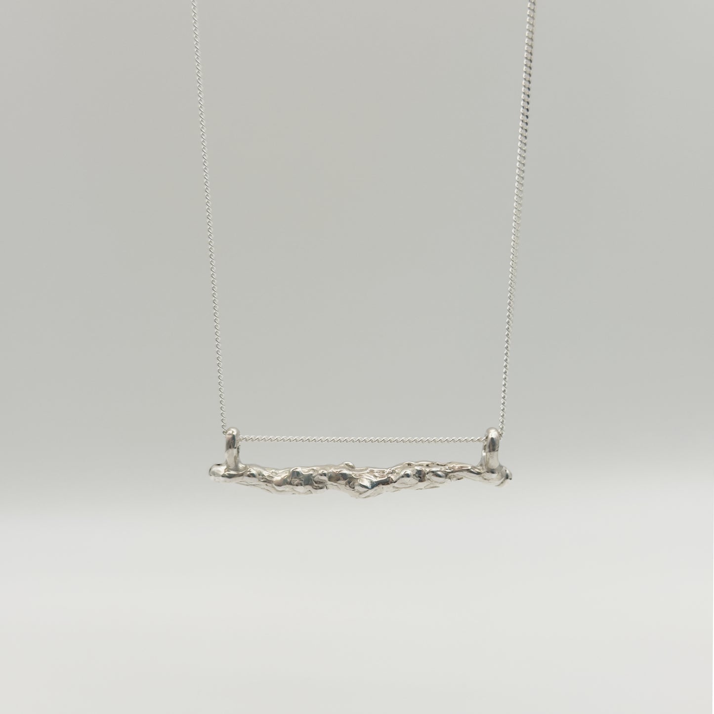 Front view of the Atoll textured silver bar pendant on a chain, pictured on a light plain background.