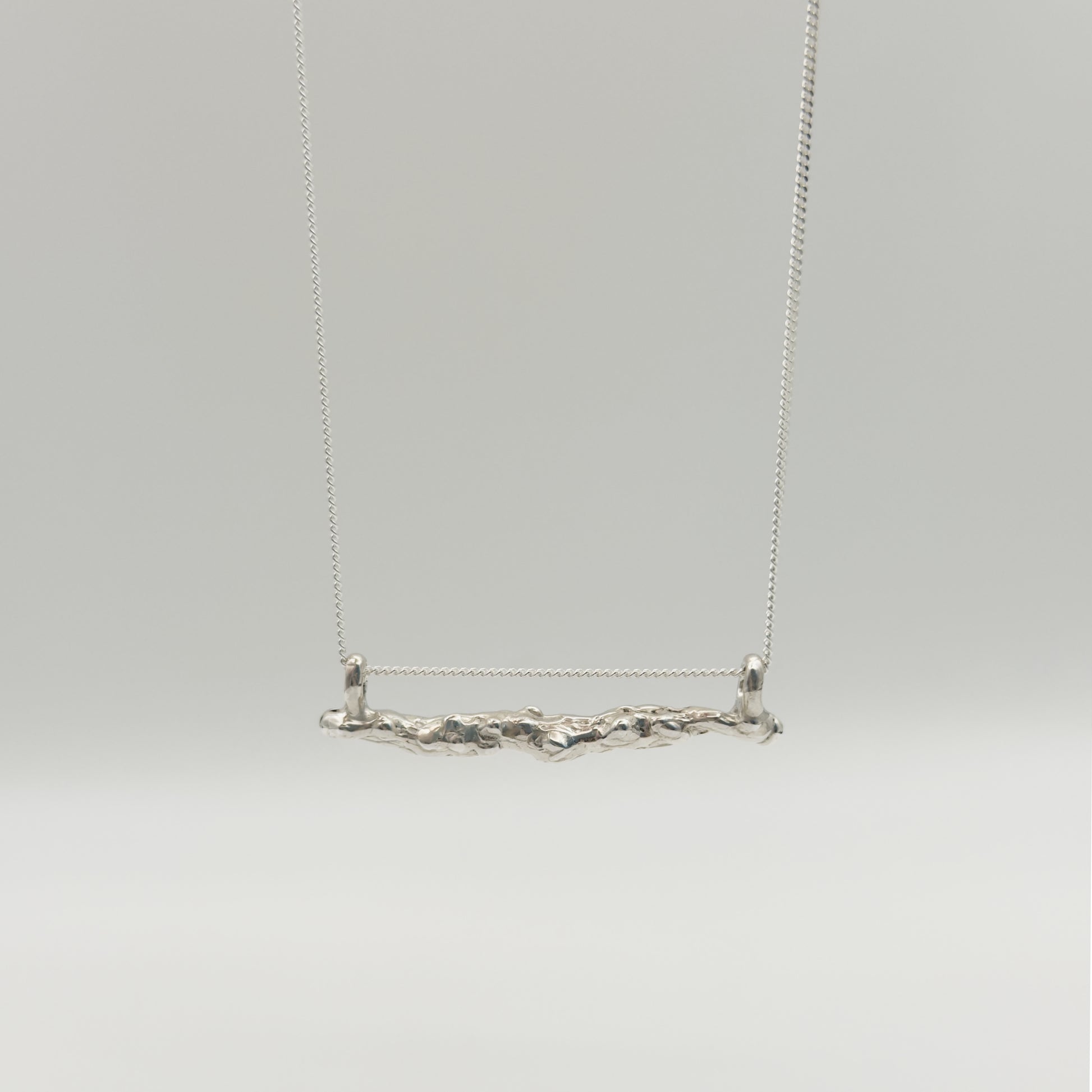 Front view of the Atoll textured silver bar pendant on a chain, pictured on a light plain background.