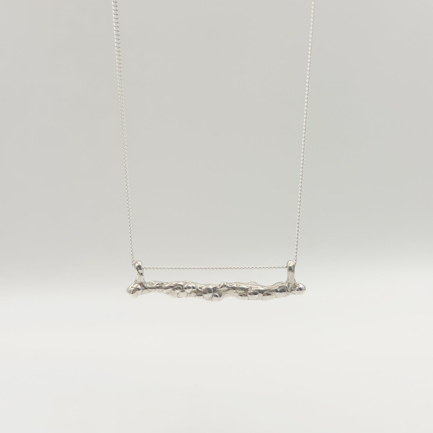 Back view of the Atoll textured silver bar pendant on a chain, pictured on a light plain background.