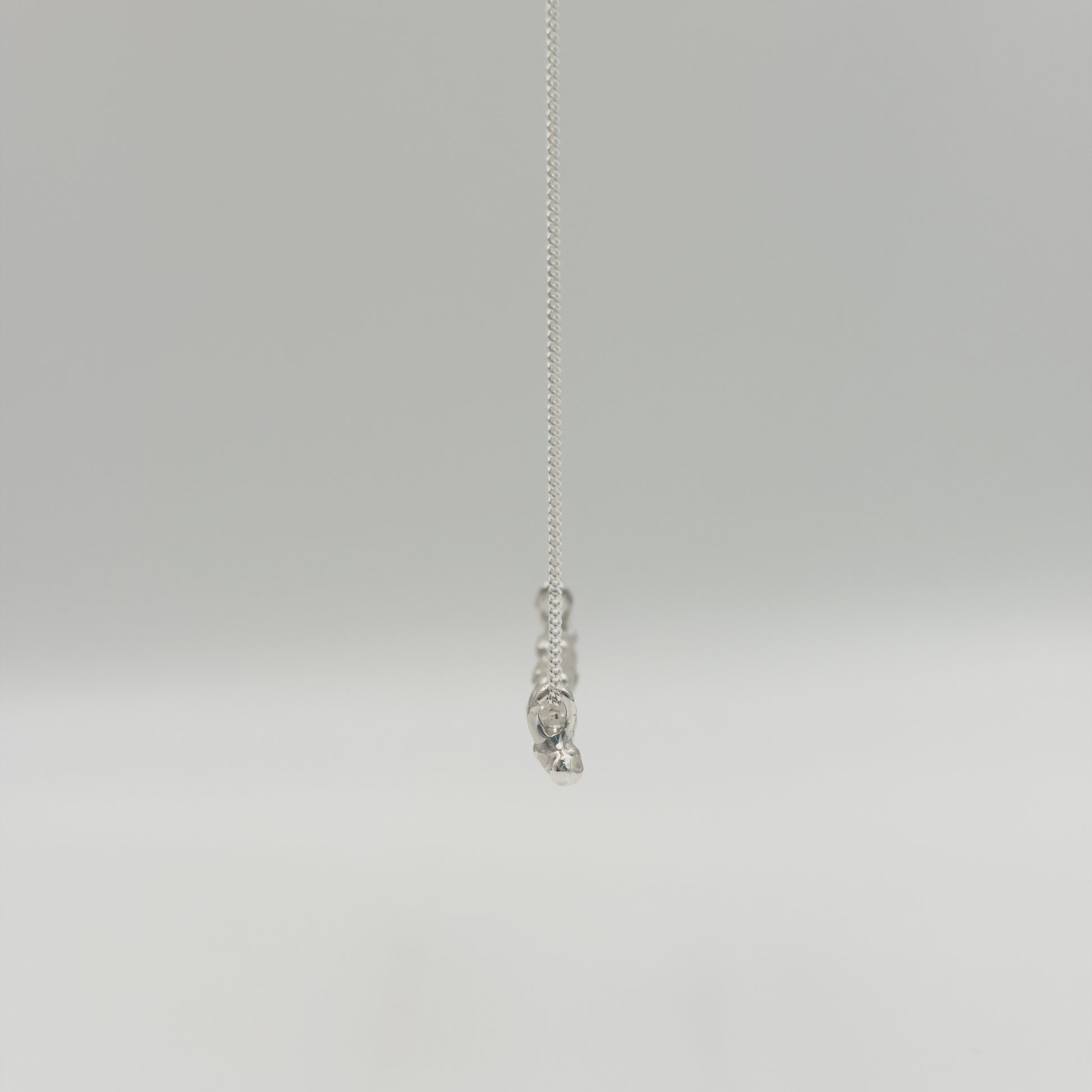 Side view of the Atoll textured silver bar pendant on a chain, pictured on a light plain background.