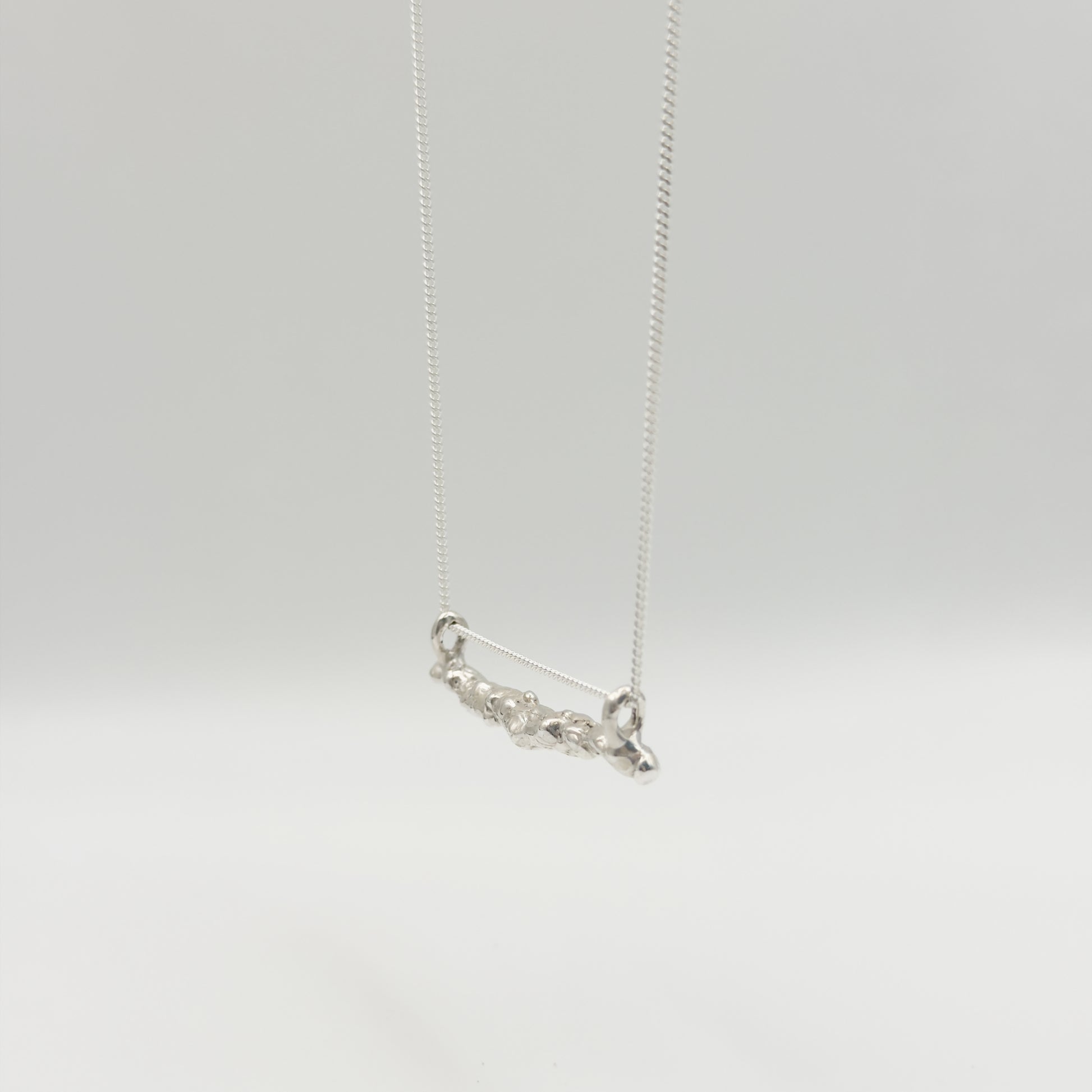 Angled front view of the Atoll textured silver bar pendant on a chain, pictured on a light plain background.