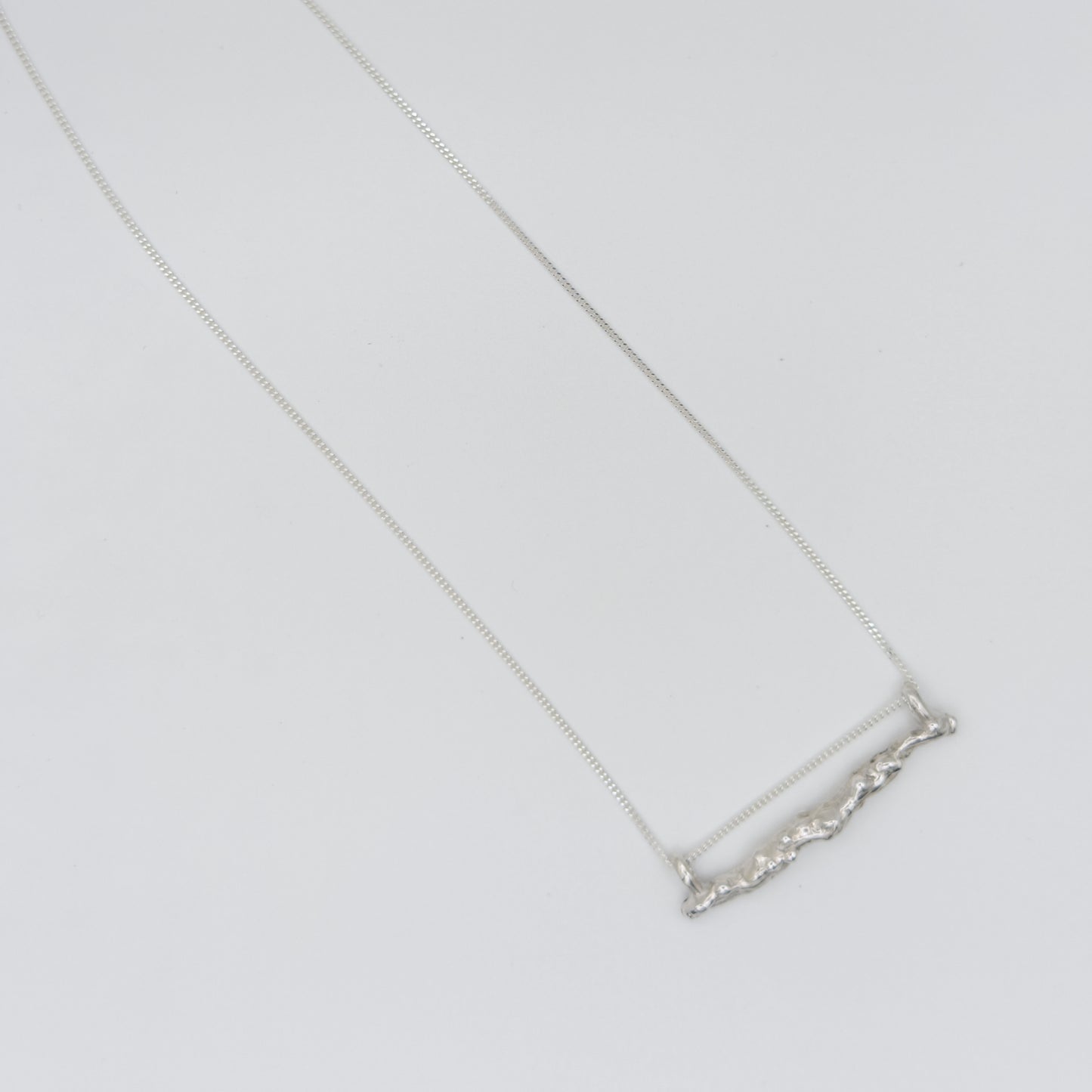 Top view of the Atoll textured silver bar pendant on a chain, pictured on a light plain background.