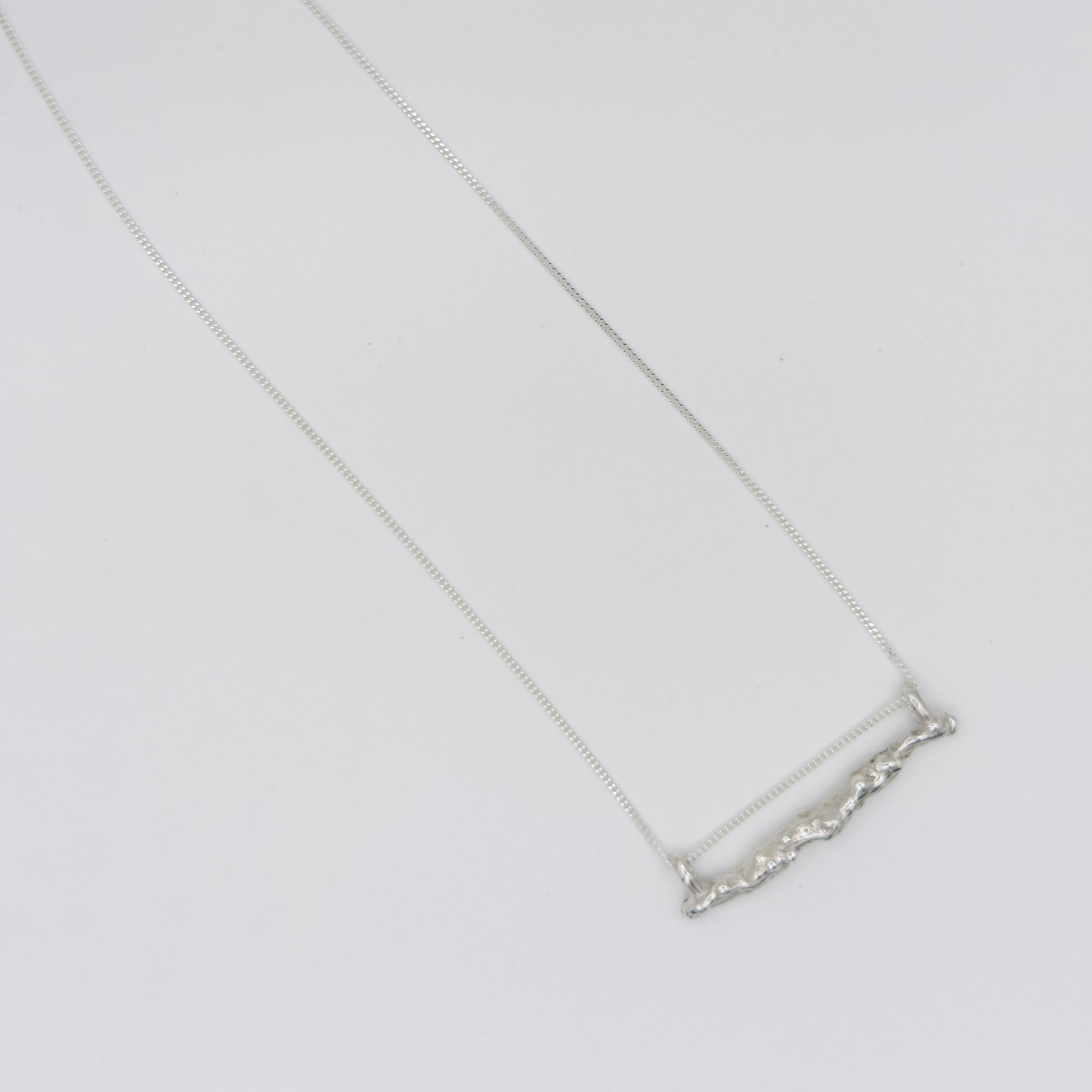 Top view of the Atoll textured silver bar pendant on a chain, pictured on a light plain background.