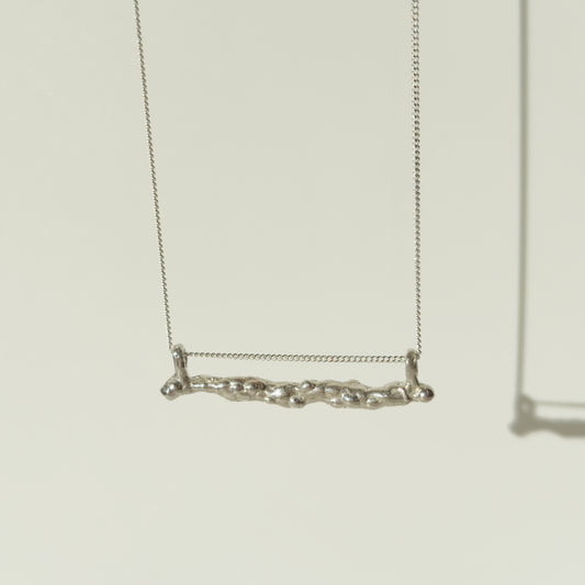Front view of the Atoll textured silver bar pendant on a chain, pictured on a light plain background.