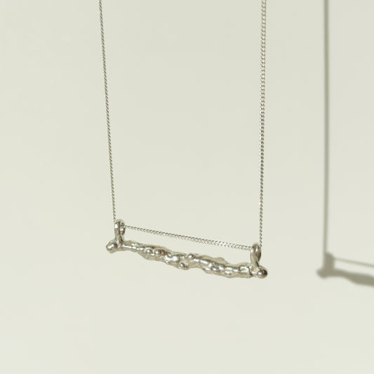 Angled front view of the Atoll textured silver bar pendant on a chain, pictured on a light plain background.
